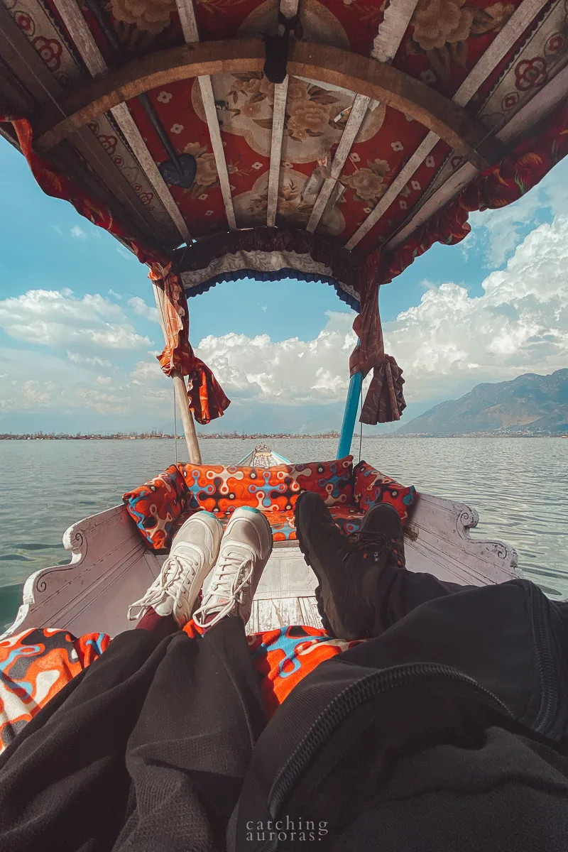 A photo of two pairs of feet wearing sneakers on a shikara ride in Dal Lake