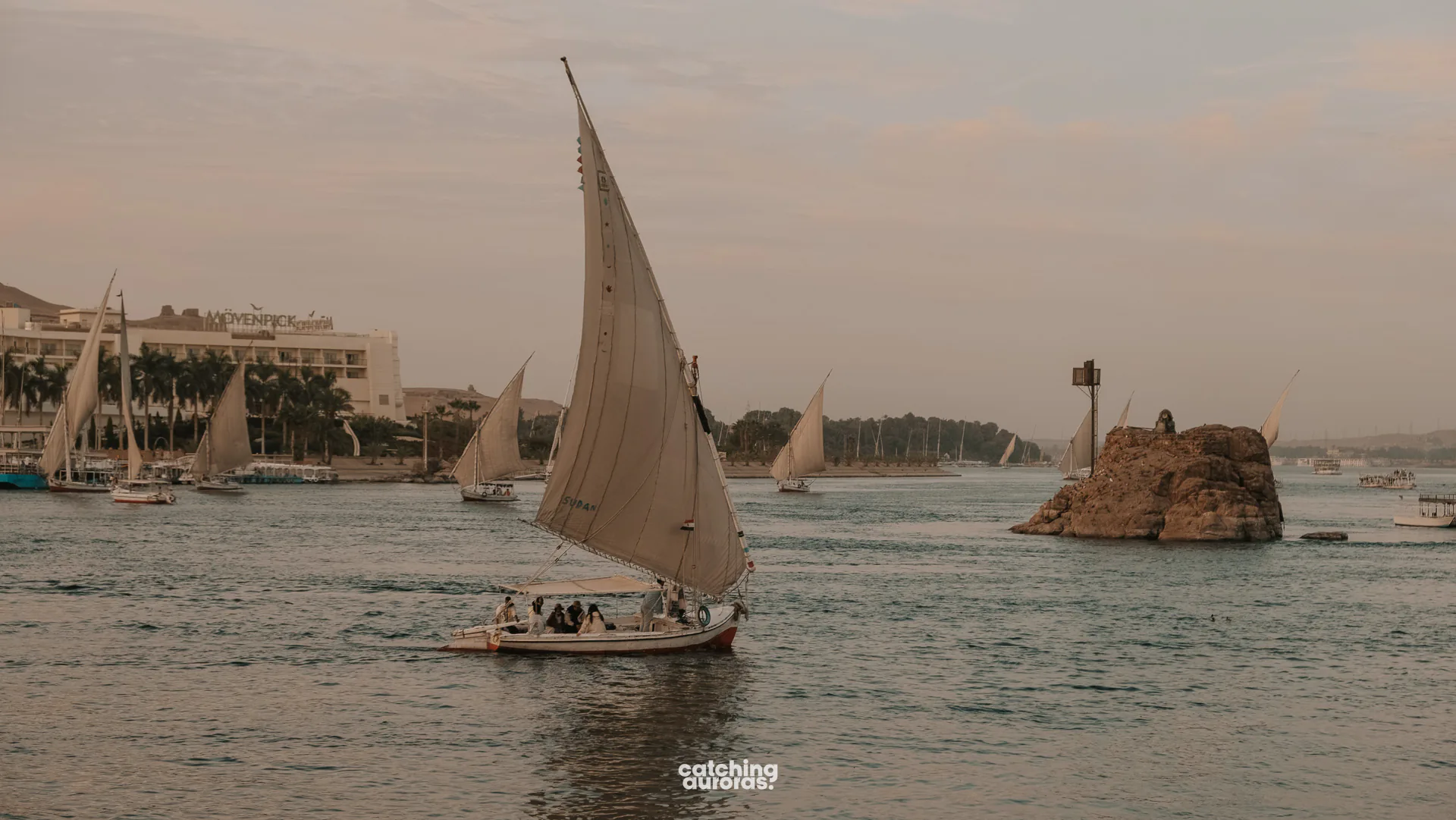 Felucca sailing on the Nile at sunset, seen from the riverbank in Aswan, Egypt.