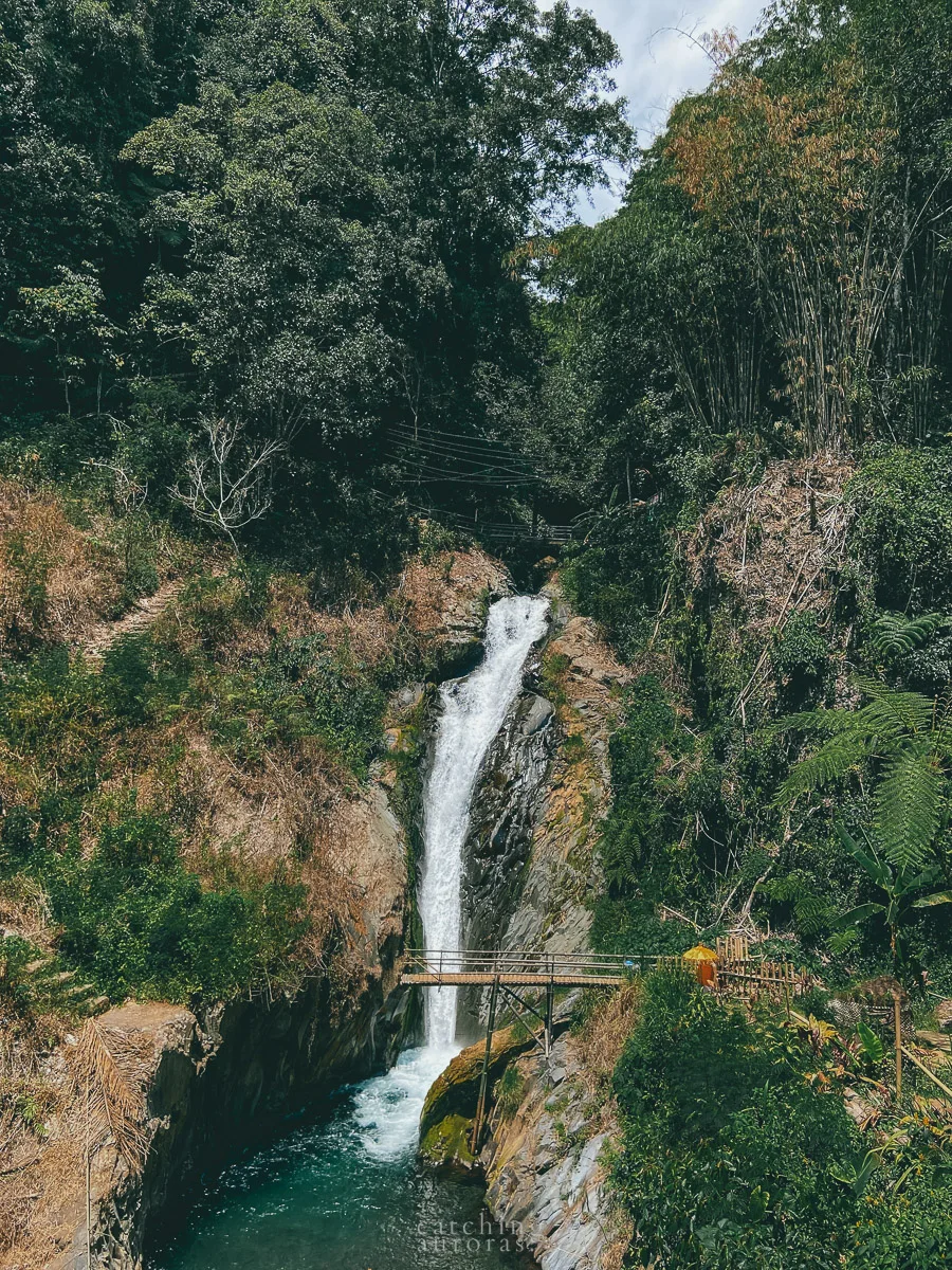 A waterfall flows down behind a broken down bridge.