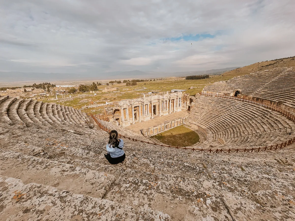 A girl wearing a blue top sits on the steps of an old Greek amphitheatre