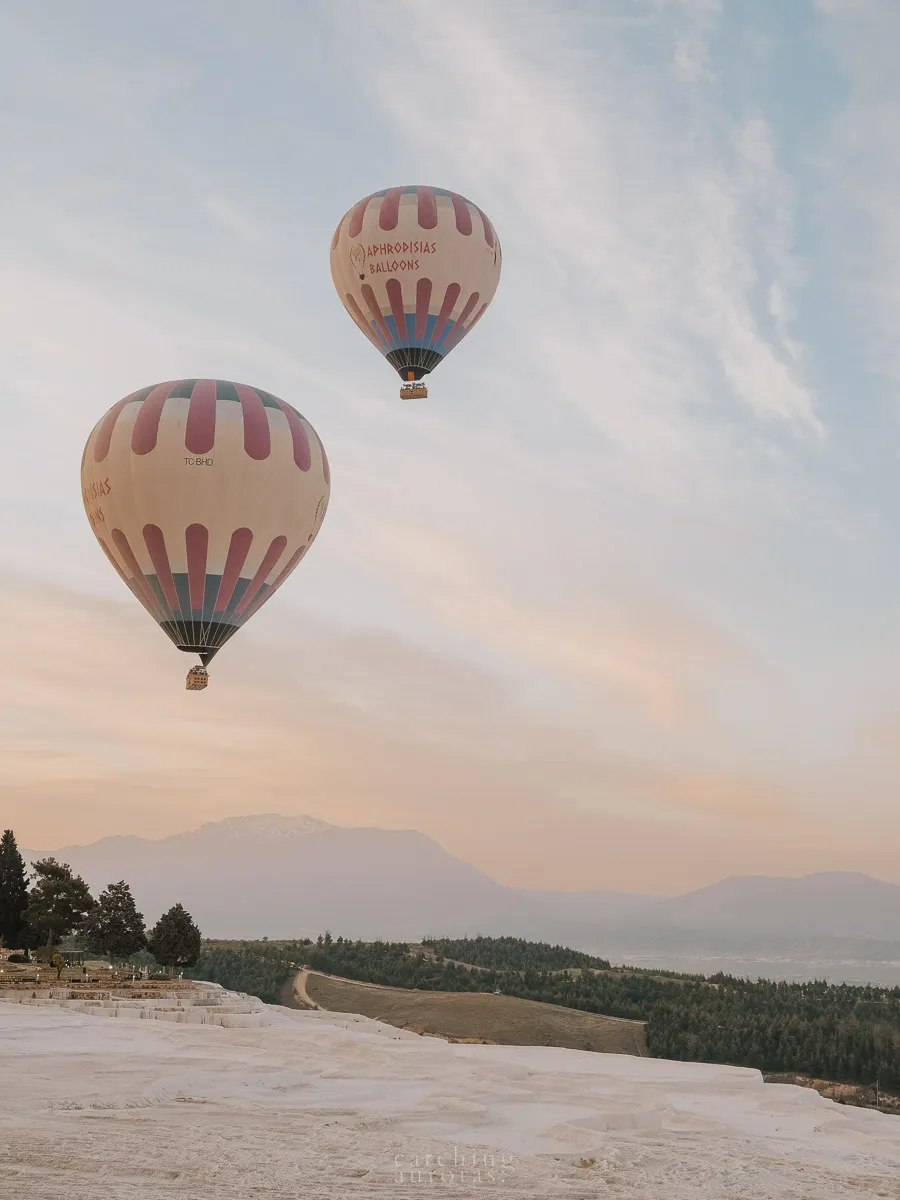 A pair of hot air balloons fly over the white terraces