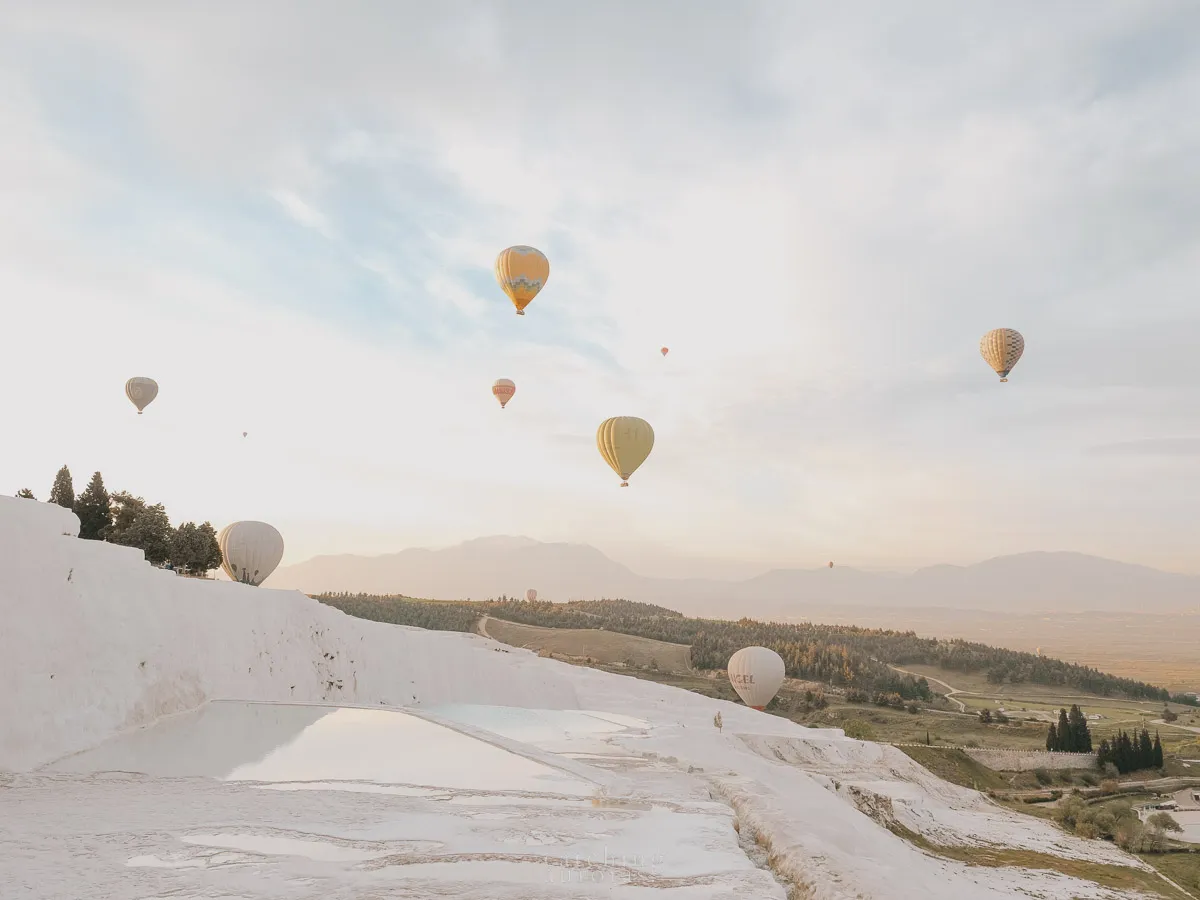 A photo of hot air balloons over white terraces with pools of water