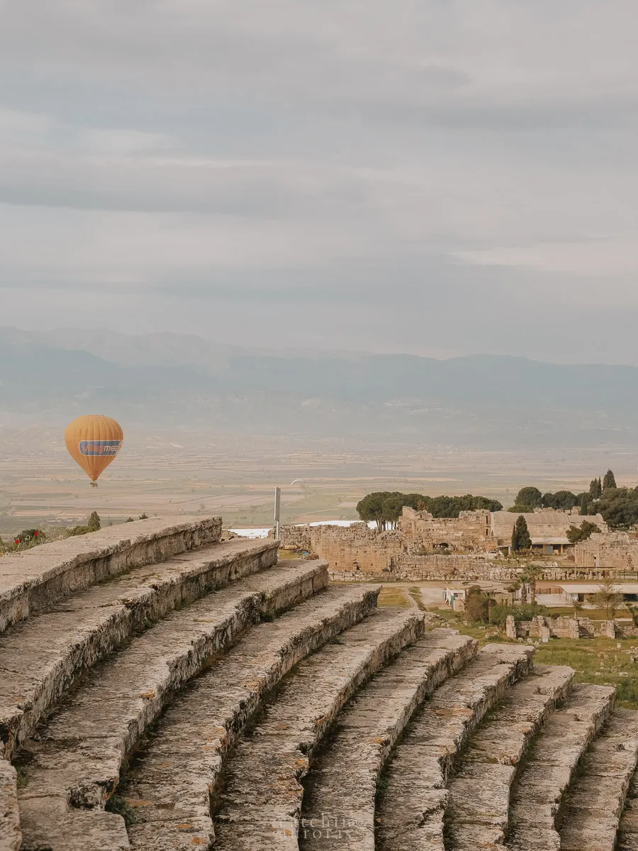 A hot air balloons rises over the steps of an ancient greek amphitheatre