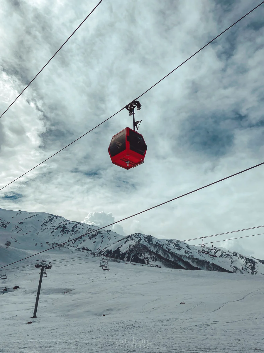 A red gondola hangs above a snowy mountain side