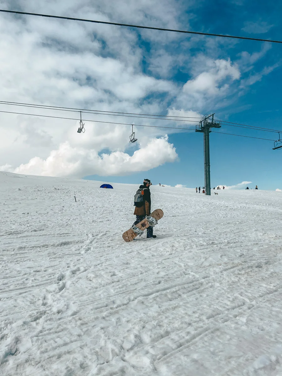 A man carrying a snowboard walks over a snow filled peak