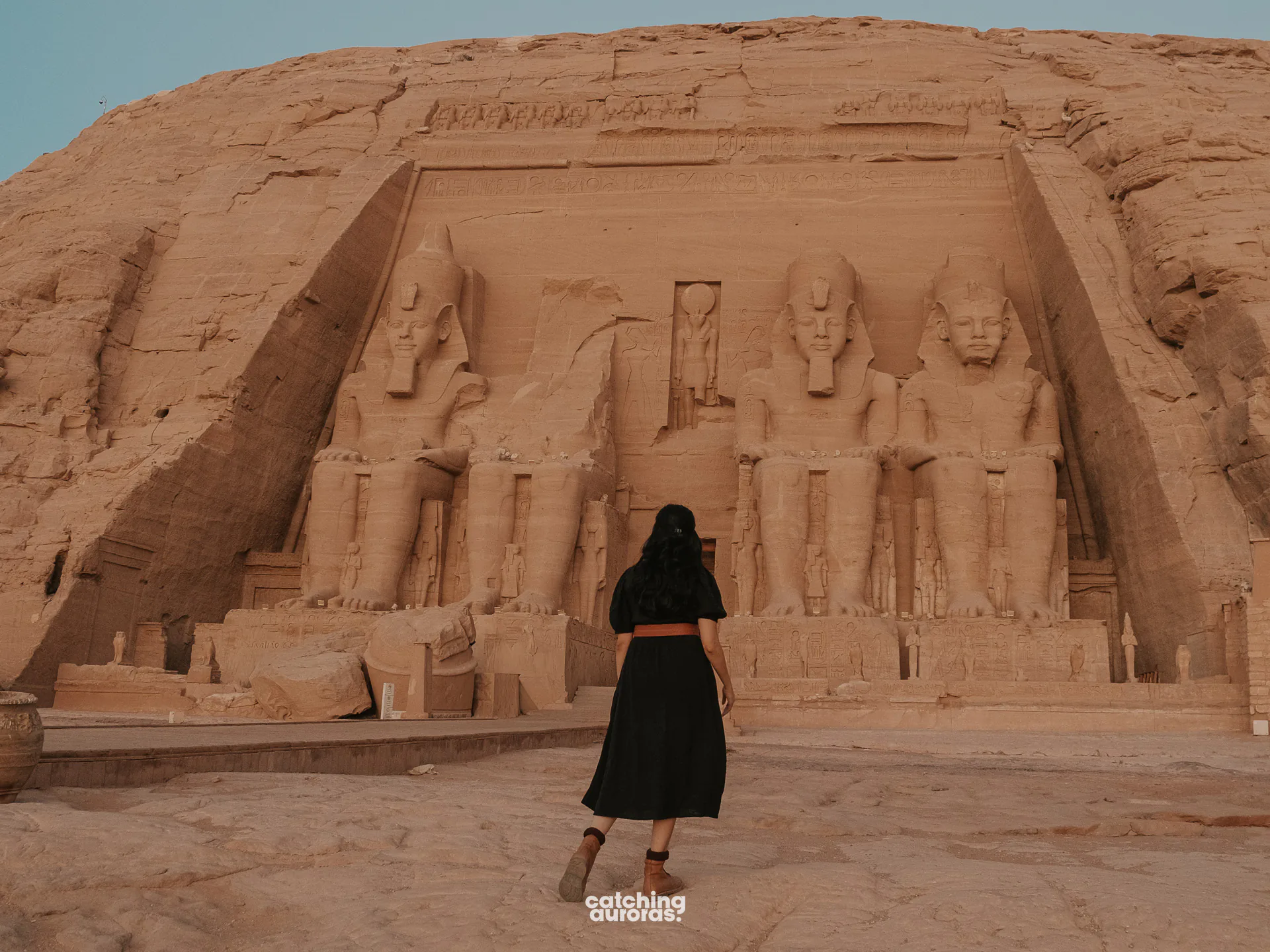 Traveller in a black dress looking up at the seated colossi of the Great Temple