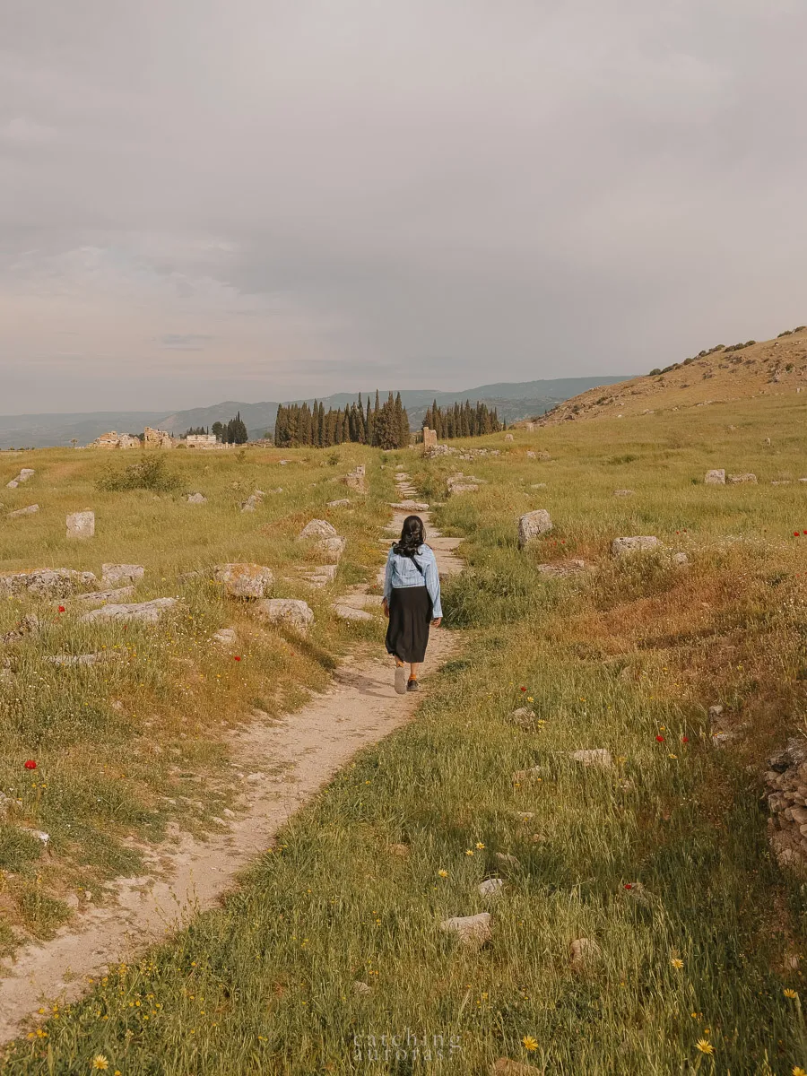 A girl walks on a path in the middle of a green field in Hierapolis